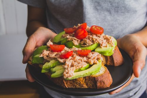 Person Holding A Sandwich With Tuna And Sliced ​​Avocado On Tomato