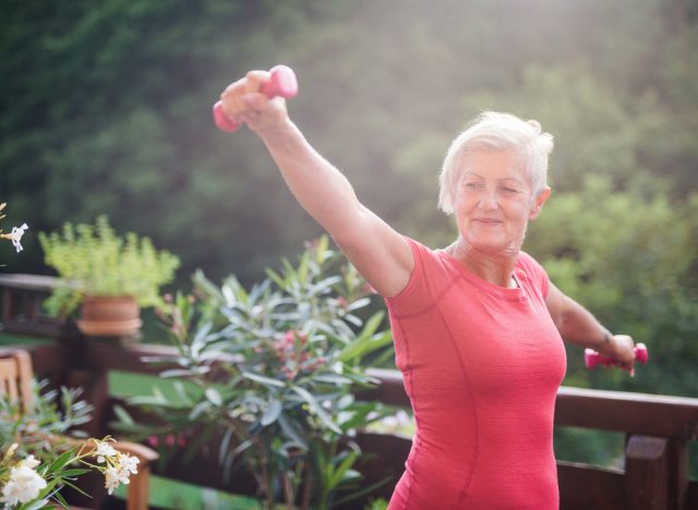 Older Woman Holding Dumbbells Exercising Outside On Her Patio