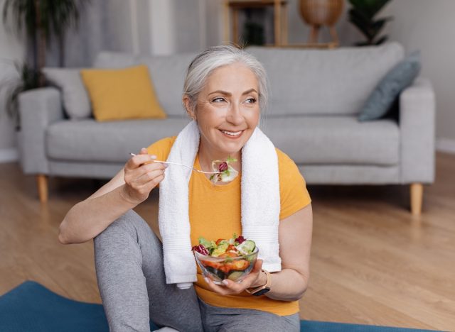 Happy fit woman eating salad on yoga mat, concept of tips to lose weight for good