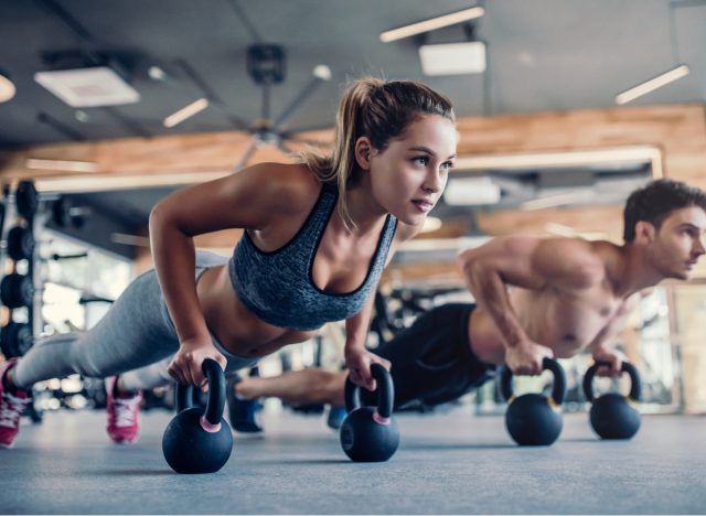 fitness couple doing kettlebell push ups fat burning exercise to lose weight at gym