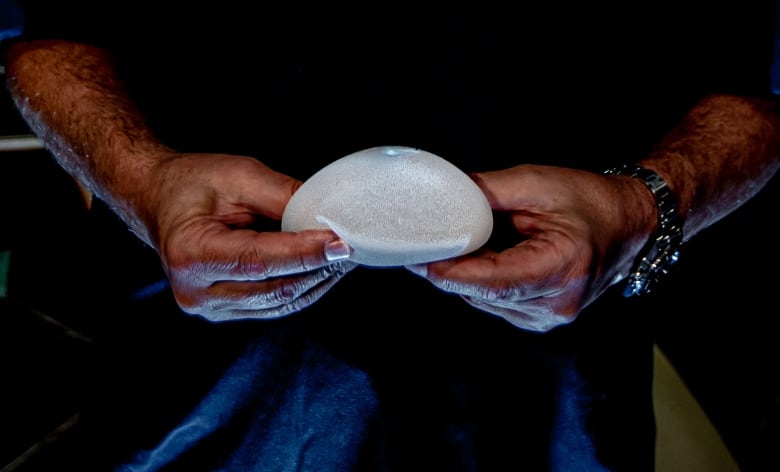 The Hands Of A Plastic Surgeon In A Blue Coat Hold A Breast Implant.