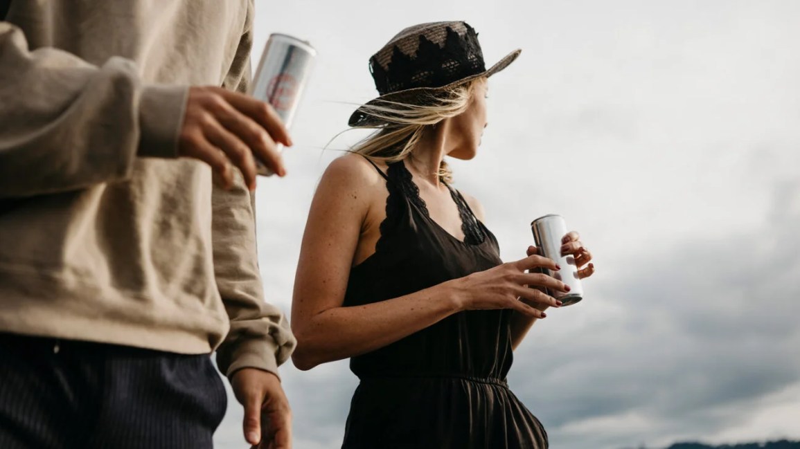 Two people drinking from cans of soda outdoors.