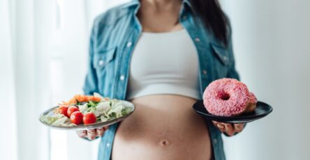 Photo of a pregnant woman choosing between vegetables and donuts