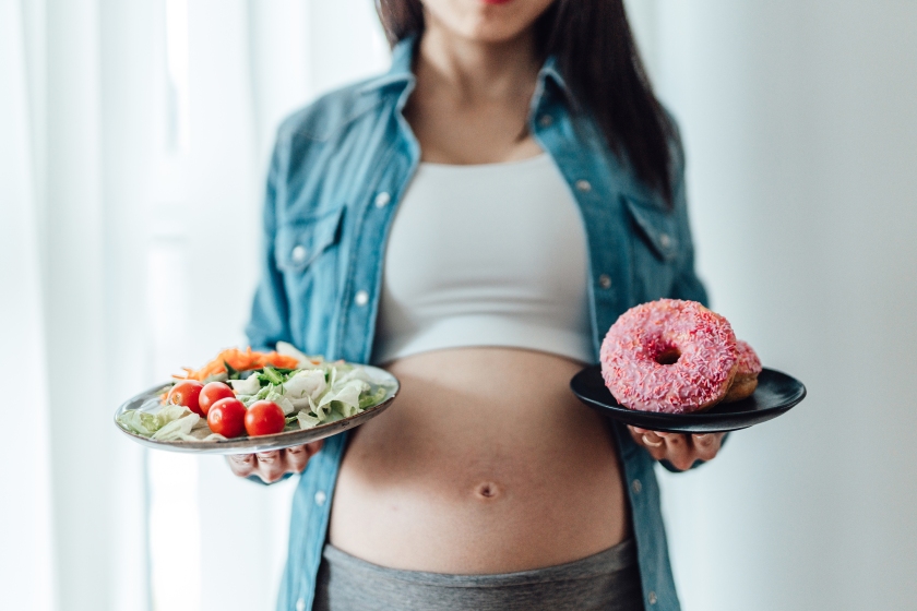 Photo of a pregnant woman choosing between vegetables and donuts